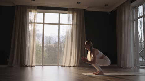 A-young-beautiful-woman-in-a-hall-with-large-windows-at-sunset-does-stretching-and-yoga-exercises-in-slow-motion-in-sunlight